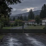 Colonia Dignidad inspired rural entrance with closed gate and distant buildings